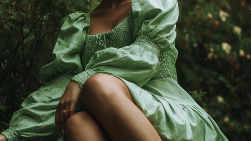 Žena u svetlo zelenoj haljini sedi u prirodi